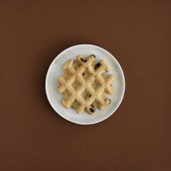 a chocolate chip waffle on a white plate on a brown background